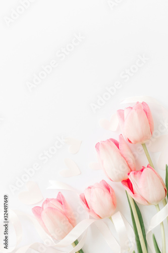 Pink tulips with ribbon and hearts on white background, flat lay. Stylish soft vertical image. Happy womens day. Greeting card mockup with space for text. Happy Mothers day. Valentines day