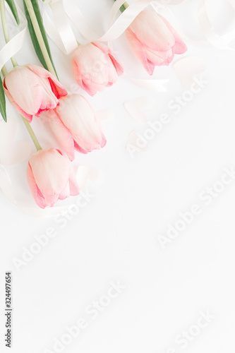 Happy womens day. Pink tulips with ribbon and hearts on white background, flat lay. Stylish soft vertical image. Greeting card mockup with space for text. Happy Mothers day. Valentines day