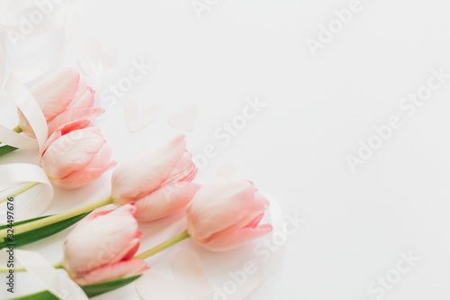 Happy Mothers day. Pink tulips with ribbon and hearts on white background. Stylish soft spring image. Happy womens day. Greeting card mockup with space for text. Hello spring