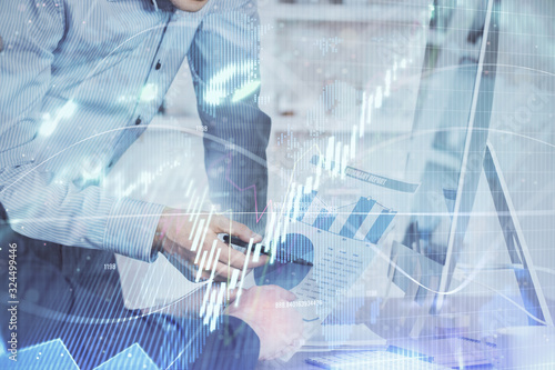 Double exposure of chart with businessman typing on computer in office on background. Concept of hard work.