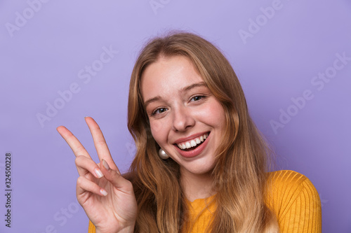 Photo of happy young woman smiling and gesturing peace sign