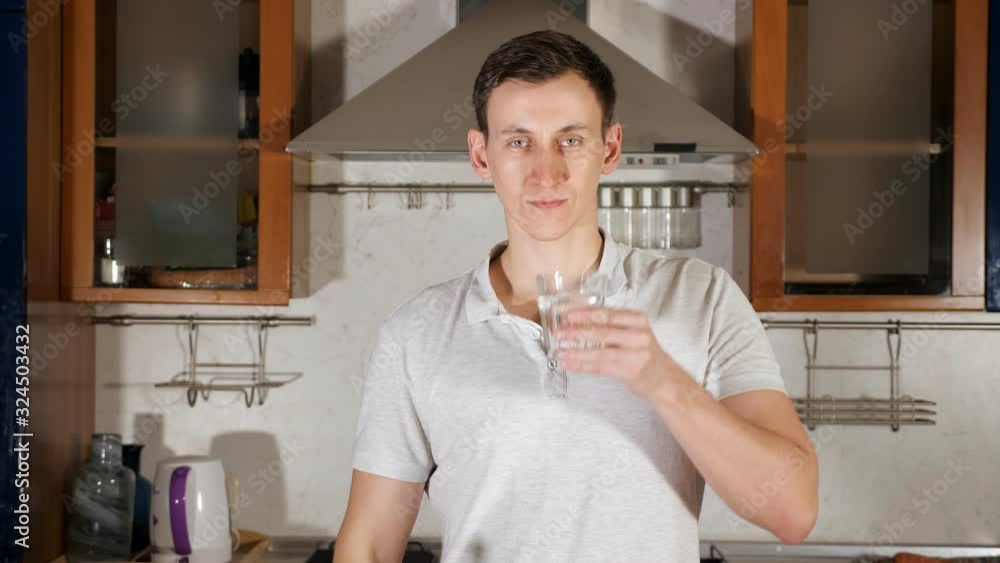 tall young man pours water into glass from bottle and drinks assuaging thirst and standing at table with vegetables close up tall young man pours water into glass from bottle and drinks assuaging thirst and standing at table with vegetables close up