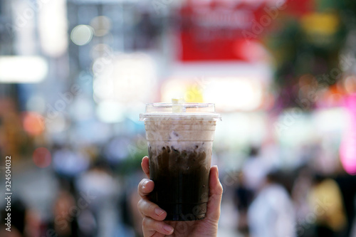 Hojicha milk tea - Hand holding plastic glass of iced milk tea with layer of cream cheese foam on blurred background and copy space, Traditional Taiwanese drink.