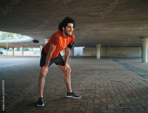 Portrait of a smiling young male athlete taking break after jogging on street relaxing under the bridge