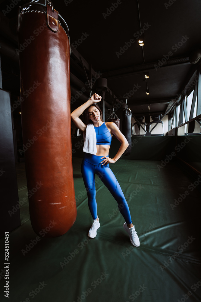 Smiling fit girl holding towel and taking rest in gym near punching bag