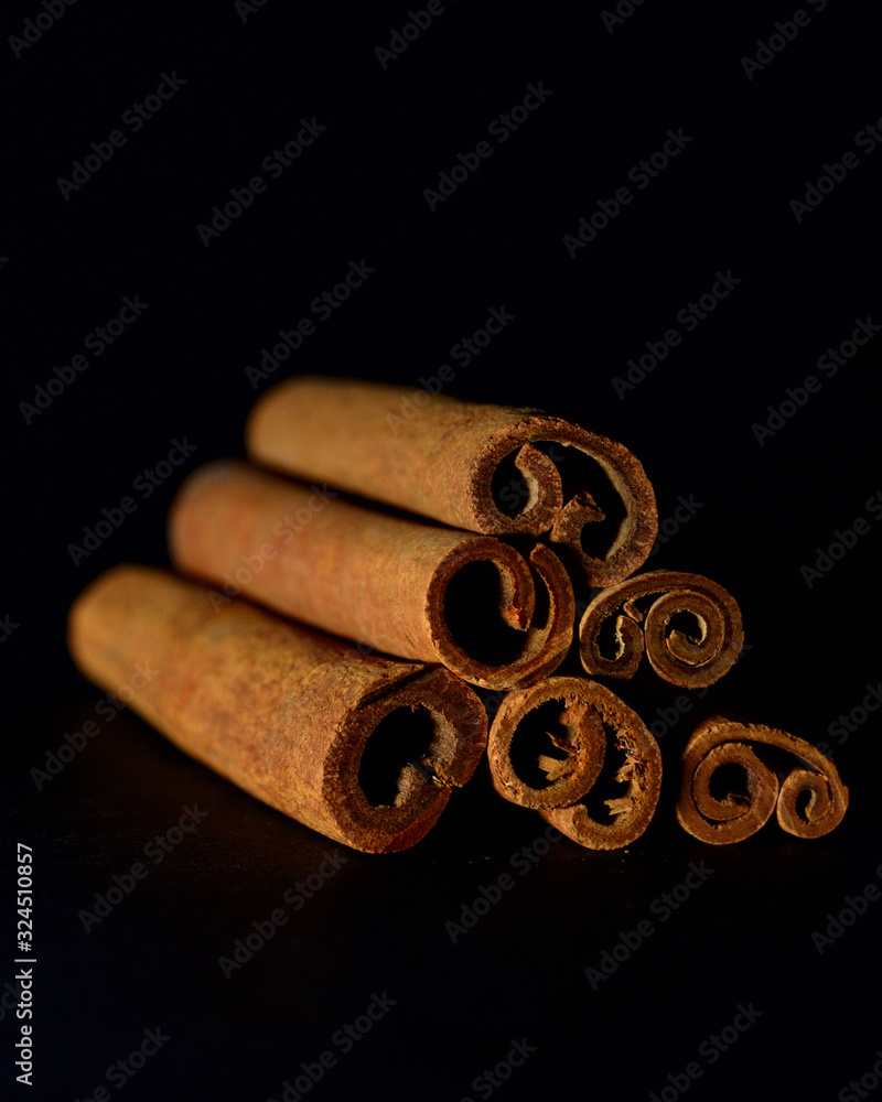Close-up of cinnamon sticks laid on top of each other by a triangle on a black blurred background