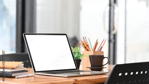 Photo of Computer laptop with white blank screen putting on wooden table together with Pencil holder, Coffee cup, Stack of books. Orderly and Comfortable workplace concept.