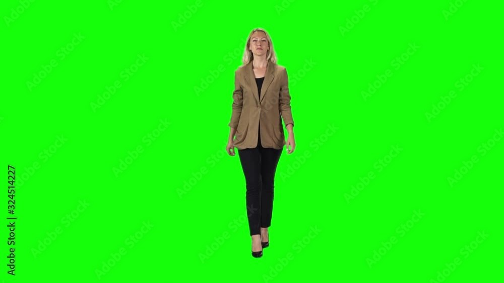 Blonde girl in a stylish brown jacket, black trousers and high-heeled shoes going against a green screen. Slow motion Blonde girl in a stylish brown jacket, black trousers and high-heeled shoes going against a green screen. Slow motion