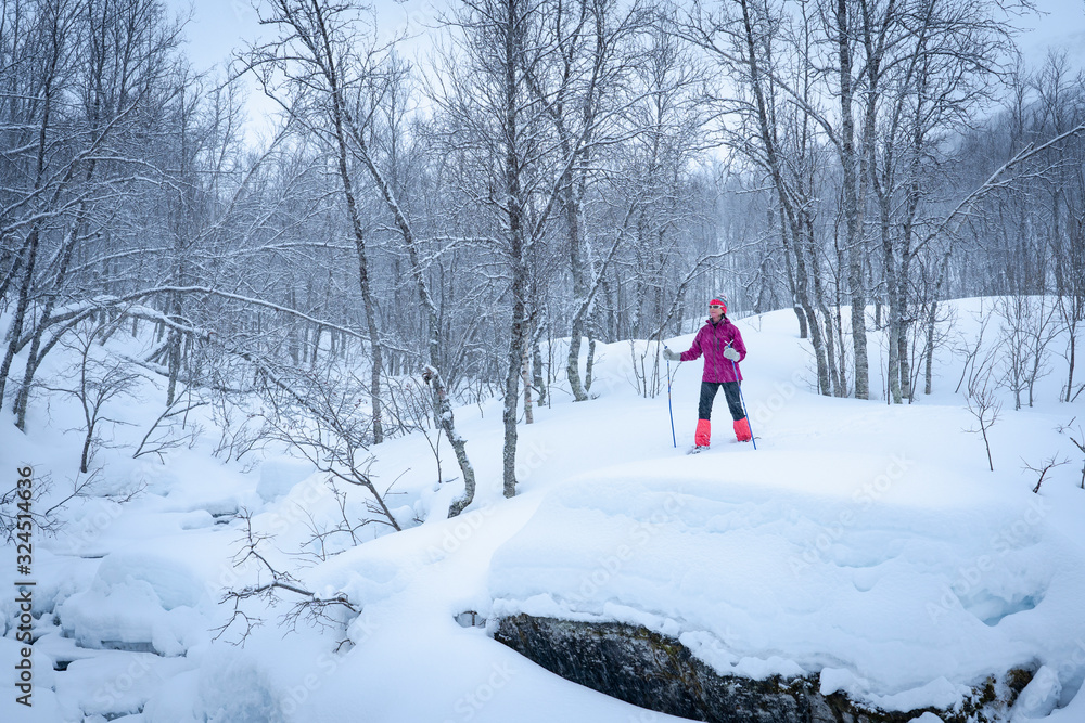 nice senior woman snowshoeing in the arctic landscaoe of northern Norway near the city of Tromso