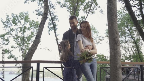 Beautiful young family on a walk, parents with daughter in a park on an alley