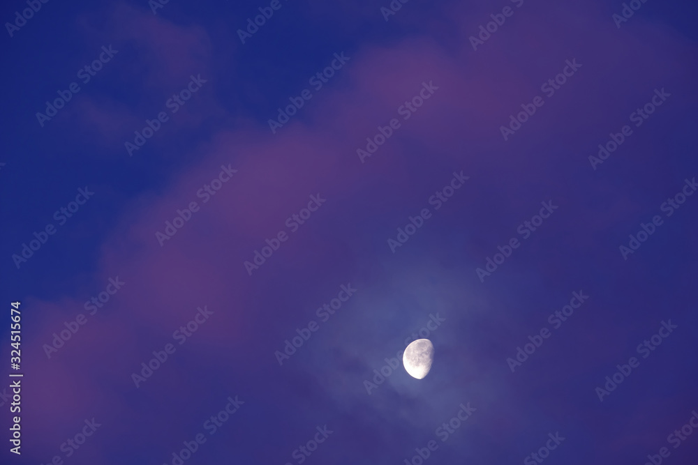 The bright moon appears behind some beautiful pink clouds on the blue sky on a winter morning in Germany The bright moon appears behind some beautiful pink clouds on the blue sky on a winter morning in Germany