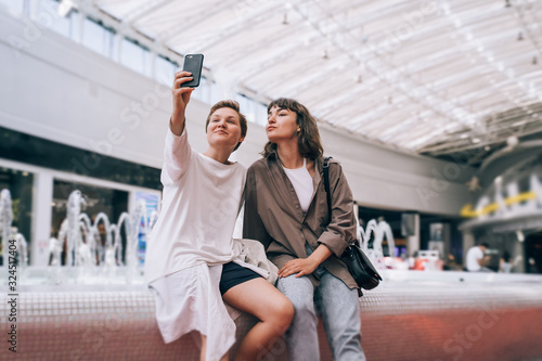 Two girls take a selfie in the mall, a fountain in the background