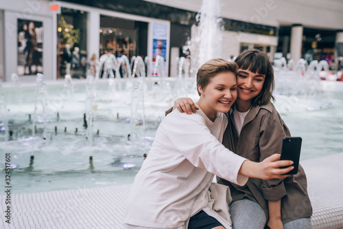 Two girls take a selfie in the mall, a fountain in the background