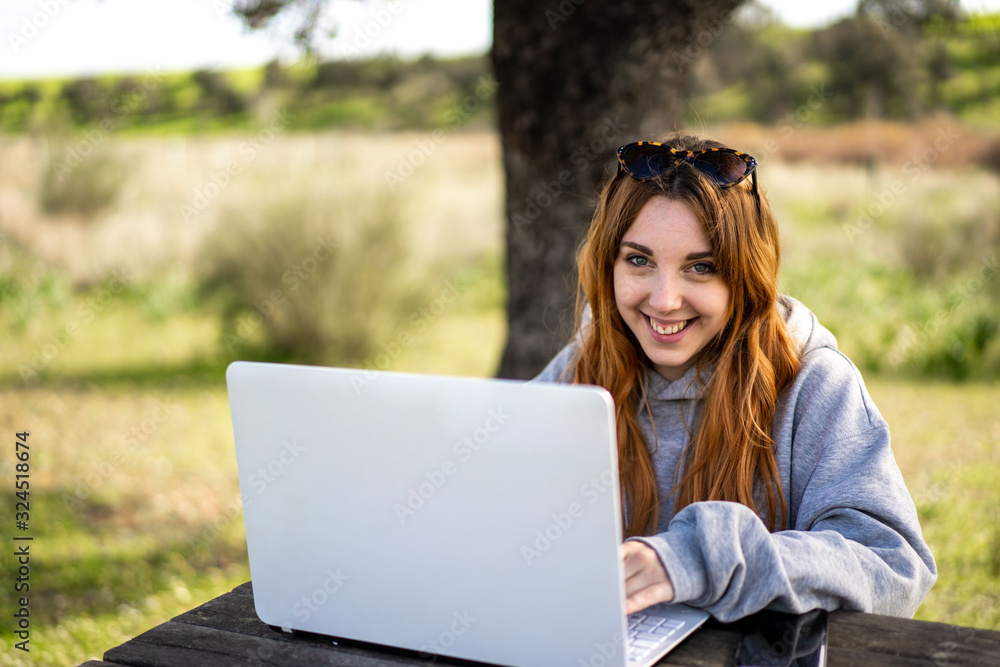 Chica joven pelirroja utiliza un ordenador portátil en el campo Chica joven pelirroja utiliza un ordenador portátil en el campo