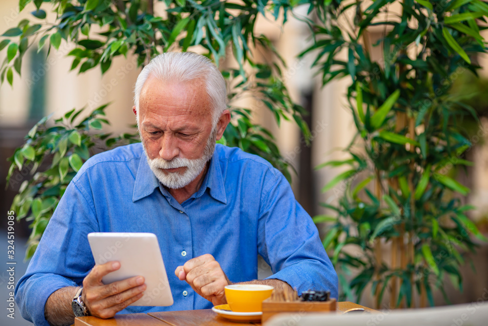 Embracing the age of the app. Mature man using a tablet in the cafe. Technology has no age limit. Making some retirement plans. Senior man reading news on digital tablet Embracing the age of the app. Mature man using a tablet in the cafe. Technology has no age limit. Making some retirement plans. Senior man reading news on digital tablet