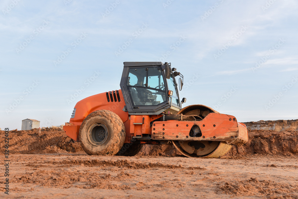 Vibration single-cylinder road roller leveling the ground for the foundation. Soil Compactor for laying asphalt on road at construction site. Road compaction equipment Vibration single-cylinder road roller leveling the ground for the foundation. Soil Compactor for laying asphalt on road at construction site. Road compaction equipment