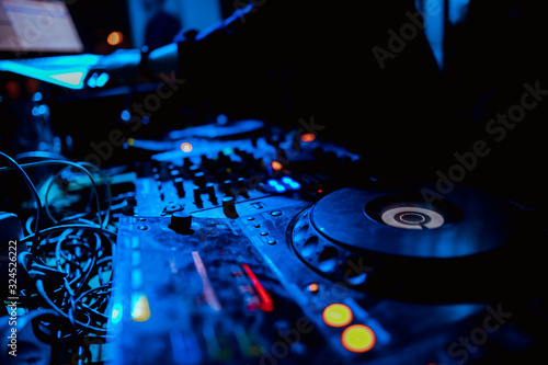 Club DJ playing mixing music on vinyl turntable at party wearing sunglasses with lens flare from nightlife lights.