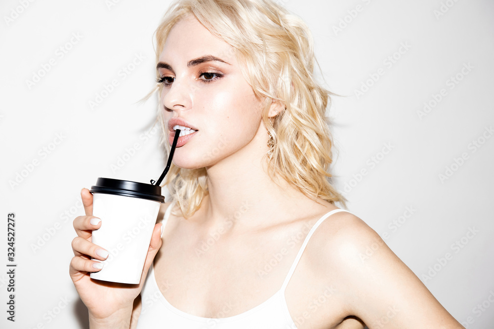 cute young blonde girl drinks from a paper cup through a straw on a white background, studio fashion photo cute young blonde girl drinks from a paper cup through a straw on a white background, studio fashion photo