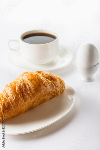 Breakfast. Croissant, coffee and soft-boiled egg. High key. Selective focus.