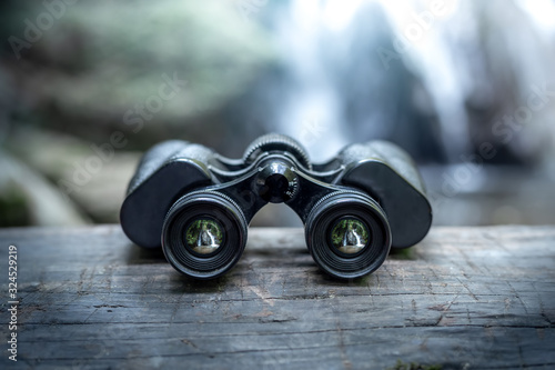 Close up binoculars on wood in forest with the waterfall behind. photo