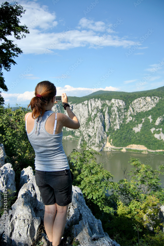 Naklejka premium Young girl taking shots with her new digital photographing camera outdoors in the nature, sunny day