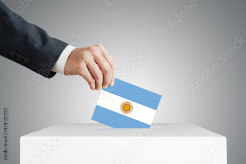 Man putting a voting ballot into a box with Argentina flag.