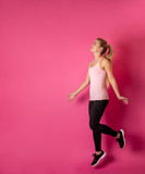 Young fit woman jumping on pink background with copy space