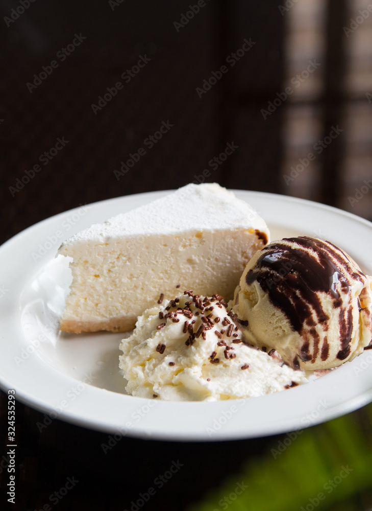 A slice of cheese cake with ice cream and whipped cream on a white plate. A slice of cheese cake with ice cream and whipped cream on a white plate.
