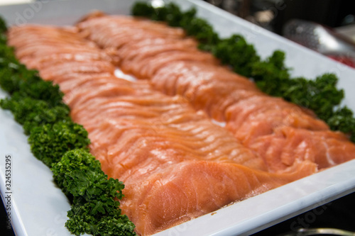 Fresh raw salmon being served on a white tray with vegetables decoration.