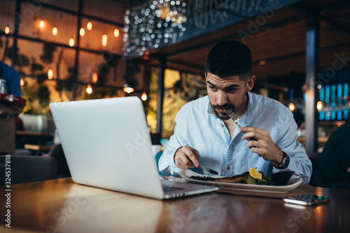 young businessman having lunch and using laptop in restaurant