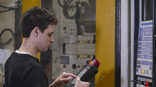 Production Worker / Machine Adjuster Adjusts the Automatic Injection Molding Machine with Teach Pendant to Start Production of Molding Housing for the Headlamps in Automotive Factory