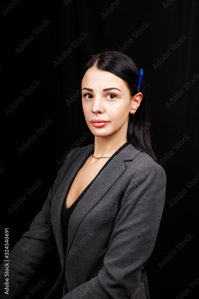 Portrait of young business woman in
a grey jacket on black background with pen behind the ear Portrait of young business woman in
a grey jacket on black background with pen behind the ear