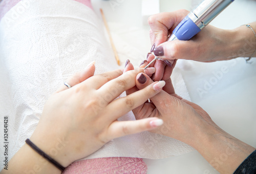 Manicure process - cleaning of nails by a milling cutter in the beauty salon  close up.