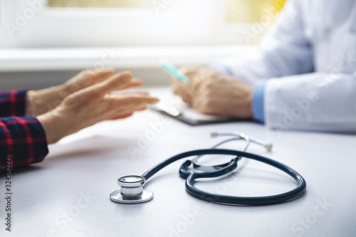 medical consultation - doctor talking to patient in clinic office. focus on stethoscope photo