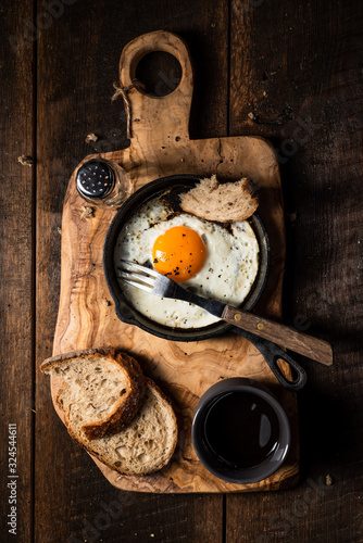 Fried egg  bread slice and black coffee.Chopping board. Dark  wooden  rustick table. Overhead view.