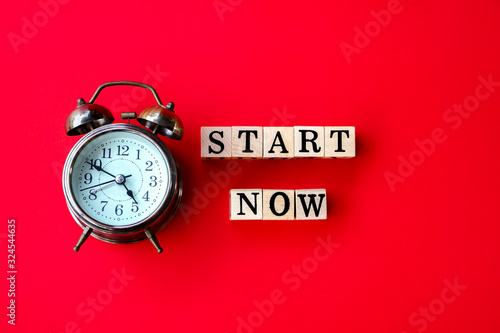 Obraz na płótnie start now concept with text on wooden block and alarm clock on red background