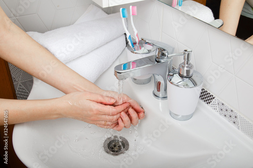 Everyday morning hygiene. Woman wash her hands. Bath preparation. White interior of bathroom. Toothbrush and soap dispenser. Details of bathroom. Personal care. Measures against infection and virus
