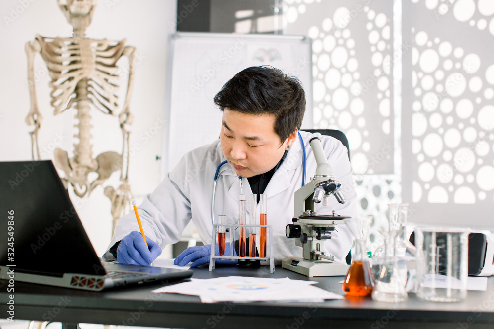 Young Asian Korean male virology scientist makes notes, working on development of new vaccine or medicine to prevent and treat new type of corona virus. Medicine, healthcare, virology concept Young Asian Korean male virology scientist makes notes, working on development of new vaccine or medicine to prevent and treat new type of corona virus. Medicine, healthcare, virology concept