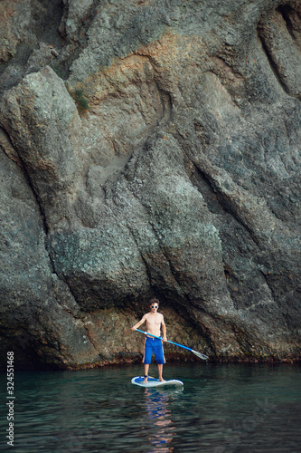 Stand Up Paddling in the sea. SUP. Guy Training in the morning on Paddle Board near the rocks.