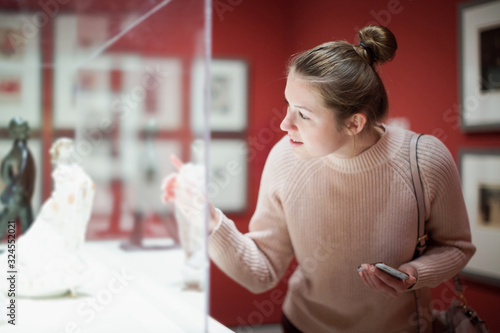 Quadro su tela Young woman visitor using  phone  in museum
