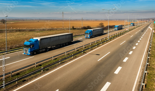 Convoy of Blue transportation trucks in line as a caravan or convoy on a countryside highway under a blue sky