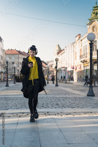Beautiful gothic girl listening her music by headphones and walking around the city