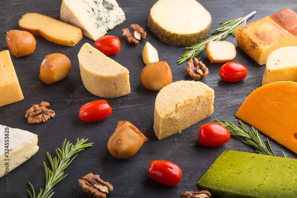 Set of different types of cheese with rosemary and tomatoes on a black wooden background . Side view.