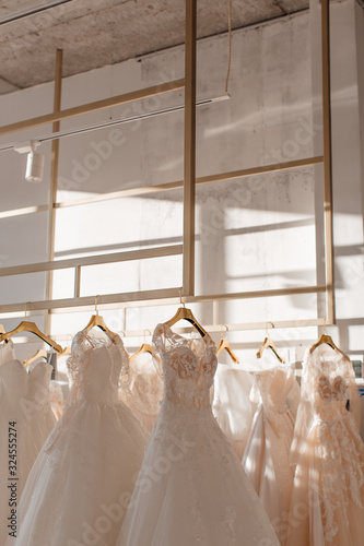 a lot of beautiful white wedding dresses on hangers in the store © Алена Ган