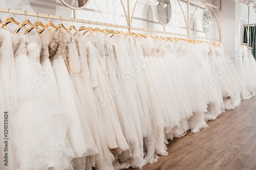 a lot of beautiful white wedding dresses on hangers in the store © Алена Ган