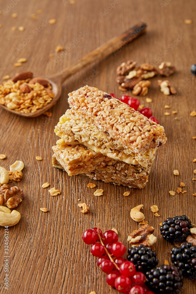 Selective focus of cereal bars, spatula with granola and redcurrants, blackberries, cashews, walnuts on wooden background Selective focus of cereal bars, spatula with granola and redcurrants, blackberries, cashews, walnuts on wooden background