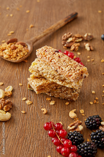 Selective focus of cereal bars, spatula with granola and redcurrants, blackberries, cashews, walnuts on wooden background