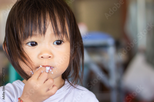 Head    shot    Portrait    image    of    1-2    years    old    of    baby.    Happy    Asian    child    girl    eating    food    rice and    eggs.    Sloppy    face.    Kid    and    food    concept.