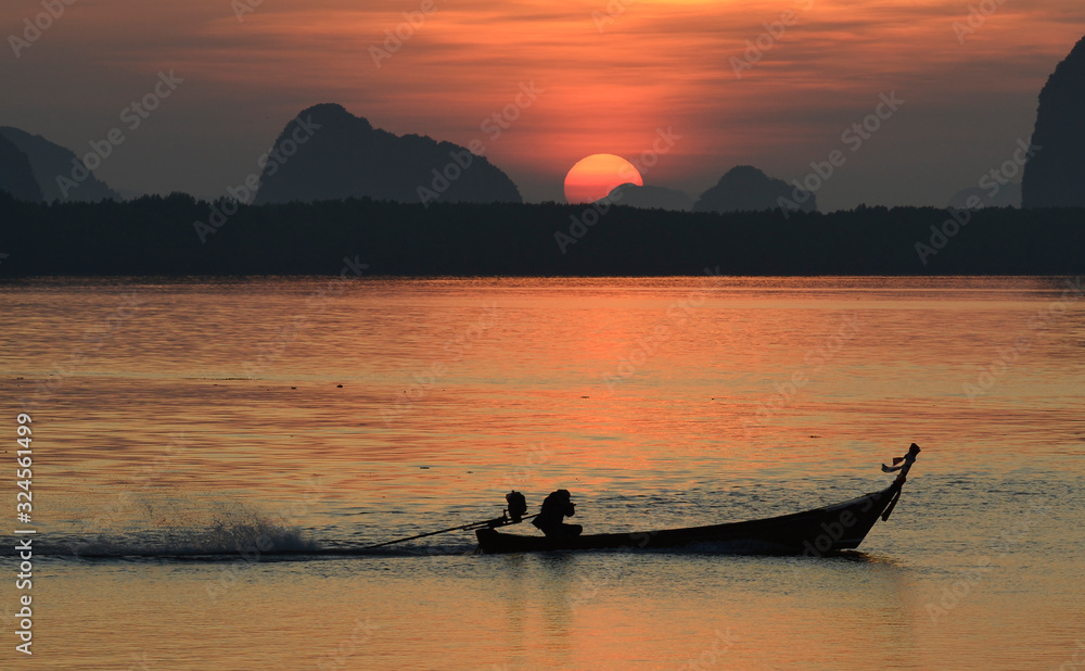 A fishing boat silhouette is sailin in a lake with sun is rising in background