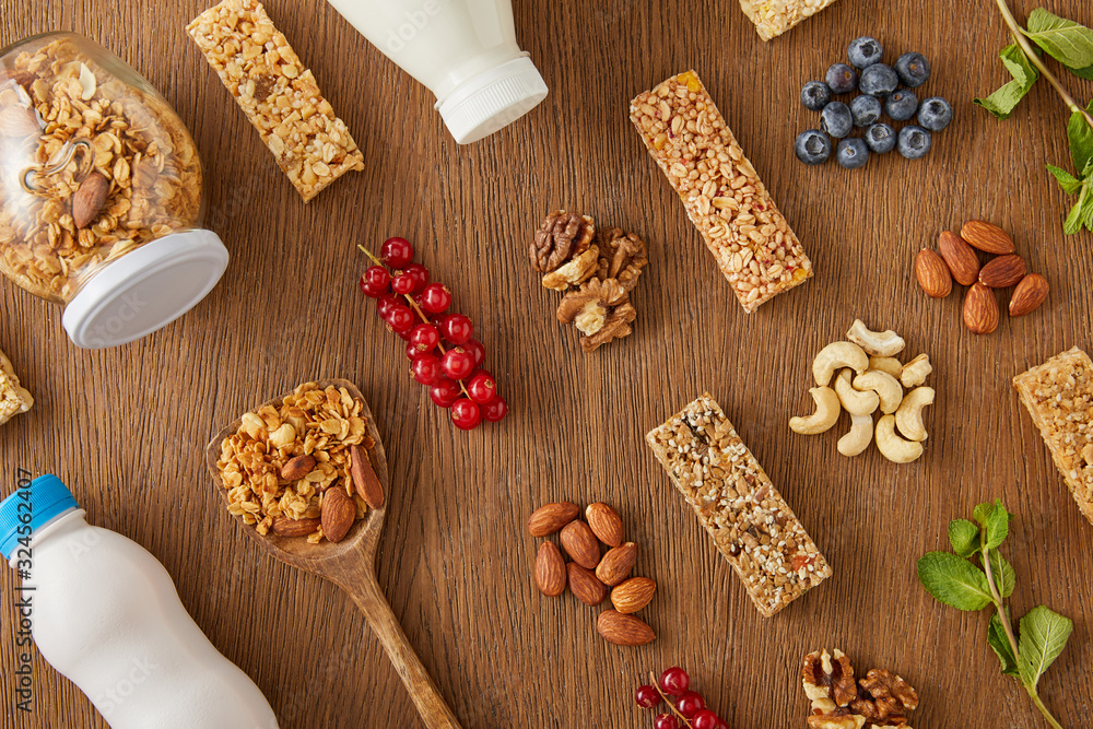 Top view of food composition of berries, nuts, cereal bars and bottles of yogurt and milk on wooden background Top view of food composition of berries, nuts, cereal bars and bottles of yogurt and milk on wooden background